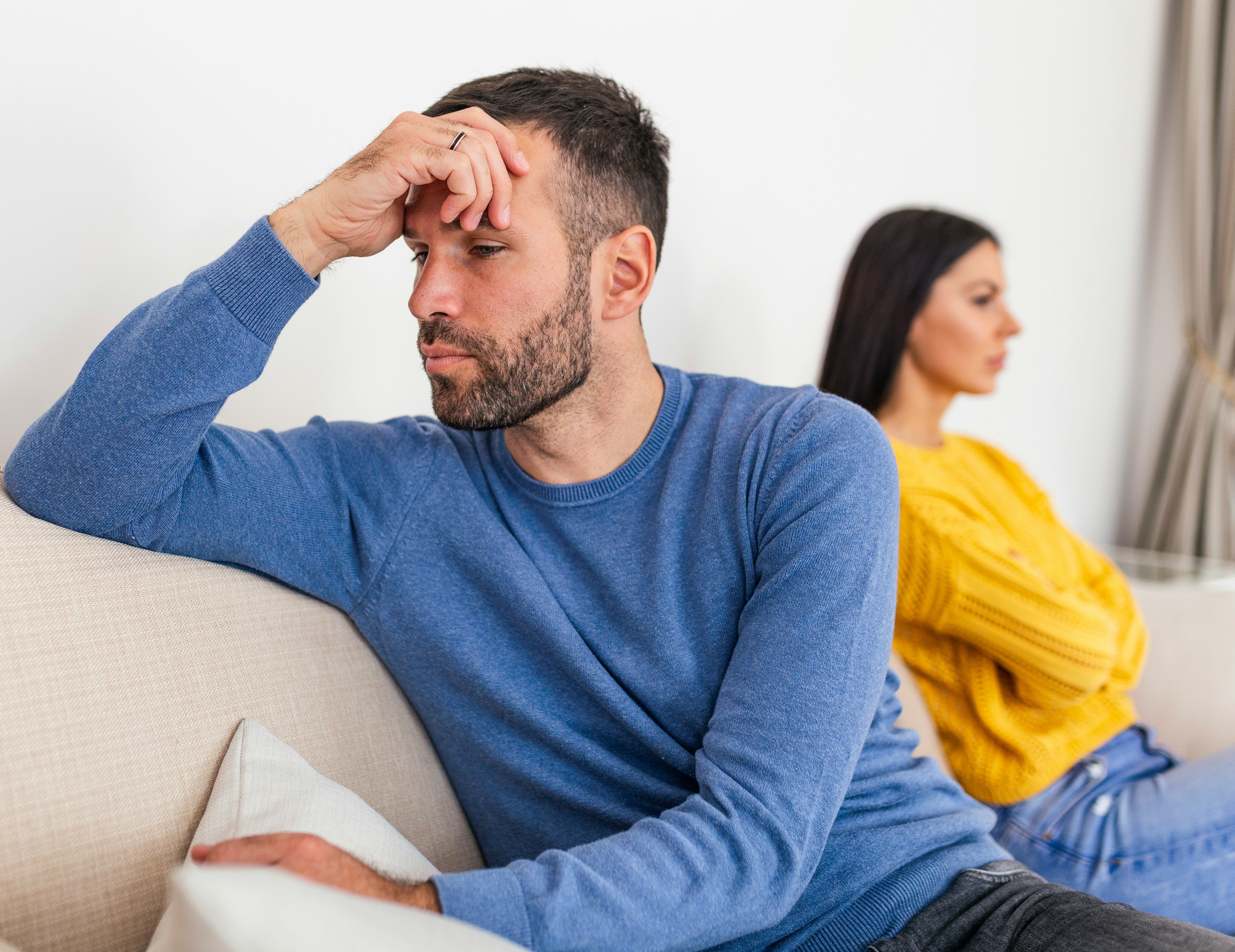 Man and woman sitting apart on a sofa, reflecting during a difficult relationship moment.